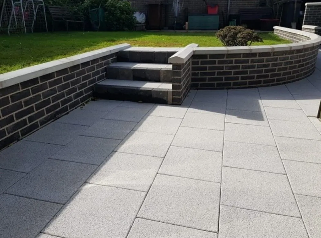 A finished sandstone patio with steps and a low retaining wall in a back garden